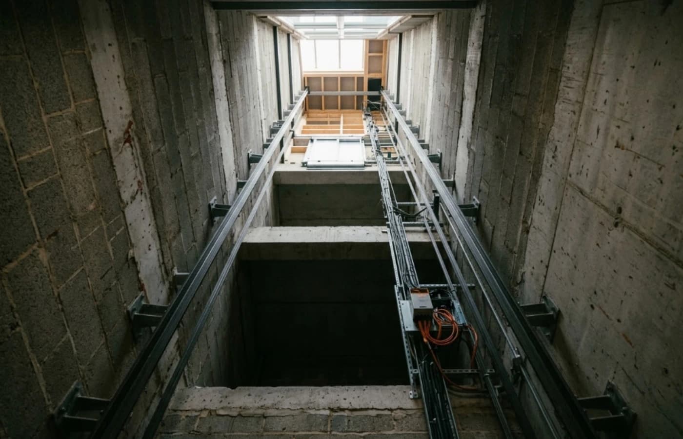 Interior view looking up through a home lift shaft during installation showing guide rails and daylight