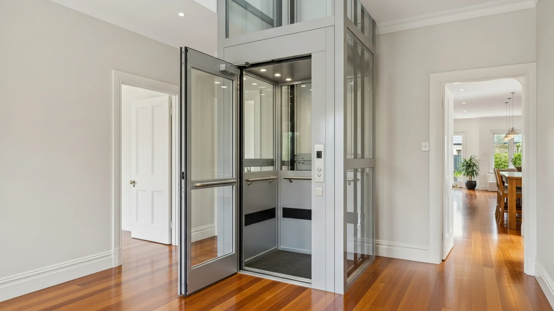 Compact through-floor home lift with glass sides passing through a rectangular aperture between the timber floors of an Australian home in soft daylight